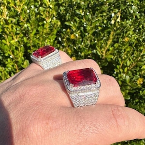 May include: Two silver rings with large red emerald-cut gemstones surrounded by smaller clear gemstones.
