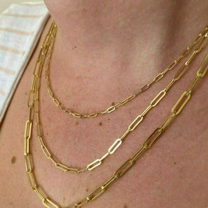 May include: Three gold chain necklaces with a paperclip link style. The chains are layered on top of each other.