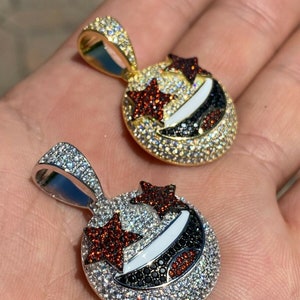 Puede incluir: Dos colgantes de oro y plata con un dise&ntilde;o de cara sonriente. Los colgantes est&aacute;n cubiertos de peque&ntilde;as piedras transparentes y rojas. La cara sonriente tiene dos estrellas para los ojos.