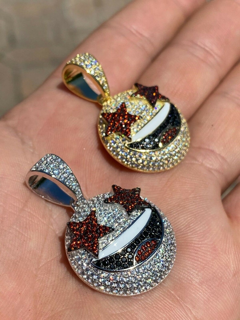 Puede incluir: Dos colgantes de oro y plata con un dise&ntilde;o de cara sonriente. Los colgantes est&aacute;n cubiertos de peque&ntilde;as piedras transparentes y rojas. La cara sonriente tiene dos estrellas para los ojos.