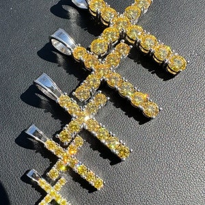 May include: Four silver cross pendants with yellow cubic zirconia stones. The crosses are different sizes and are arranged in a staggered pattern.