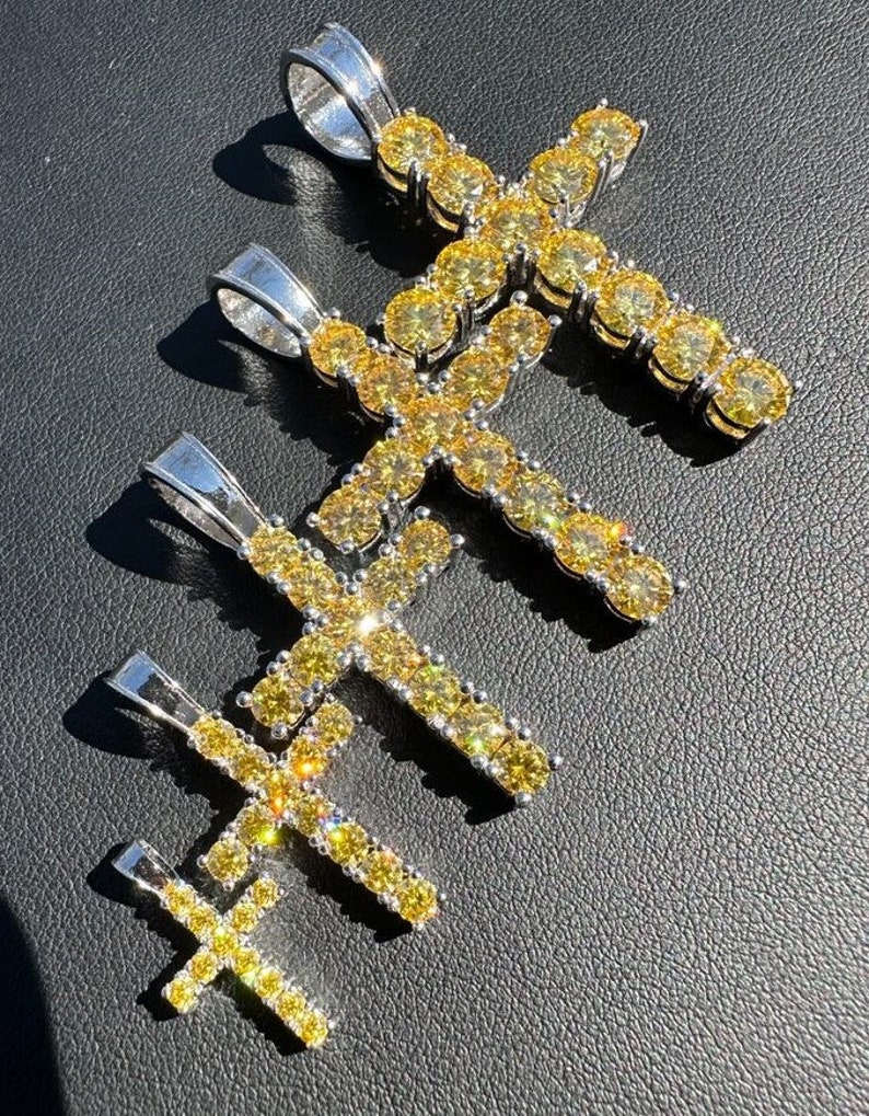 May include: Four silver cross pendants with yellow cubic zirconia stones. The crosses are different sizes and are arranged in a staggered pattern.
