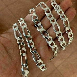 May include: A silver Figaro chain necklace with a lobster clasp. The chain is made of interlocking oval and round links.