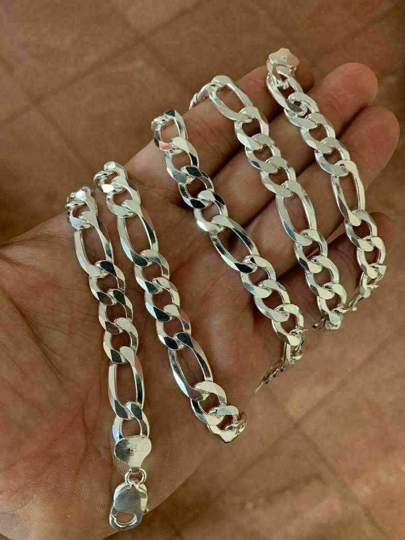 May include: A silver Figaro chain necklace with a lobster clasp. The chain is made of interlocking oval and round links.