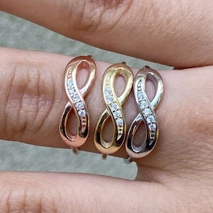 May include: Three infinity rings with small clear stones set in the band. The rings are in rose gold, yellow gold, and silver.