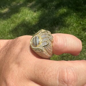 Puede incluir: Un anillo de oro con un dise&ntilde;o de mano de Hamsa, engastado con piedras de circonita c&uacute;bica transparentes.