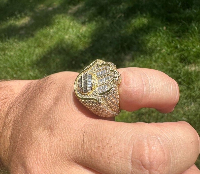Puede incluir: Un anillo de oro con un dise&ntilde;o de mano de Hamsa, engastado con piedras de circonita c&uacute;bica transparentes.
