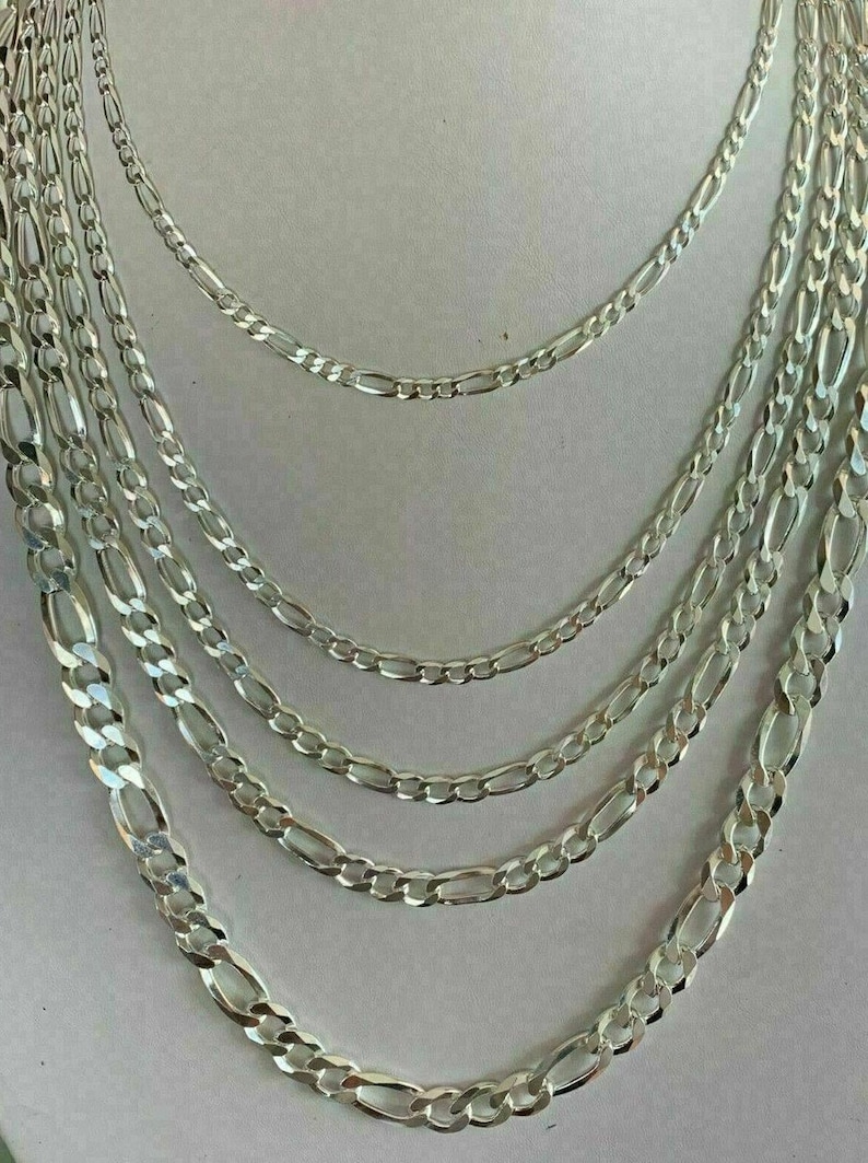 May include: A set of six silver chains with a figaro link pattern. The chains are arranged in order of size, with the largest chain at the bottom and the smallest chain at the top.