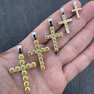 May include: Five silver cross pendants with yellow cubic zirconia stones. The crosses are different sizes, with the largest cross at the bottom and the smallest cross at the top.