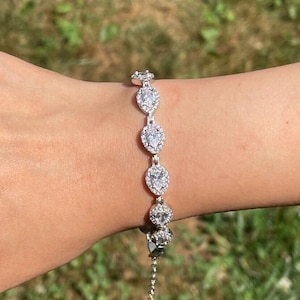 Op de afbeelding: Een zilveren armband met een ketting en peervormige stenen die zijn gezet in een halo van kleinere stenen.