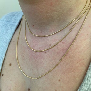 Puede incluir: Tres collares de cadena de oro superpuestos en el cuello de una persona. Las cadenas son finas y delicadas.