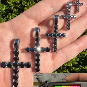 May include: Four silver cross pendants with black cubic zirconia stones. The crosses are different sizes and are held in a hand. The largest cross is 1.5 inches tall. The smallest cross is 0.5 inches tall.