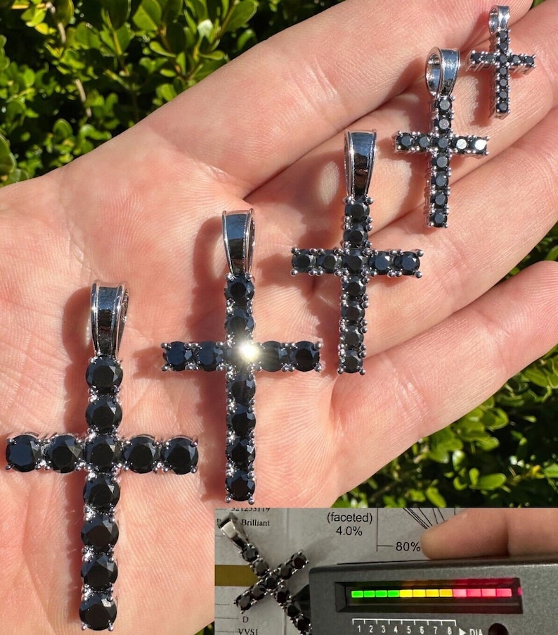 May include: Four silver cross pendants with black cubic zirconia stones. The crosses are different sizes and are held in a hand. The largest cross is 1.5 inches tall. The smallest cross is 0.5 inches tall.