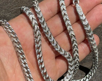 Könnte beinhalten: Eine silberne Kettenkette mit einem diamantartigen Muster. Die Kette besteht aus kleinen, ineinandergreifenden Gliedern, die ein Fischgrätenmuster bilden. Die Kette ist etwa 61 cm lang und hat einen Karabinerverschluss.