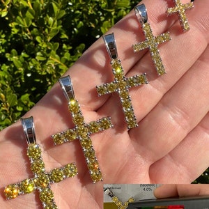 May include: Four silver cross pendants with yellow cubic zirconia stones. The cross pendants are arranged in size order from smallest to largest. The largest cross pendant is about 2 inches tall. The smallest cross pendant is about 1 inch tall. The cross pendants are on a hand.