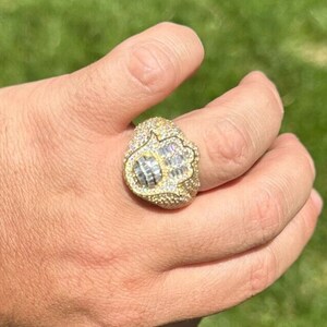 Puede incluir: Un anillo de oro con un dise&ntilde;o de mano de hamsa, incrustado con piedras de circonita c&uacute;bica transparentes.