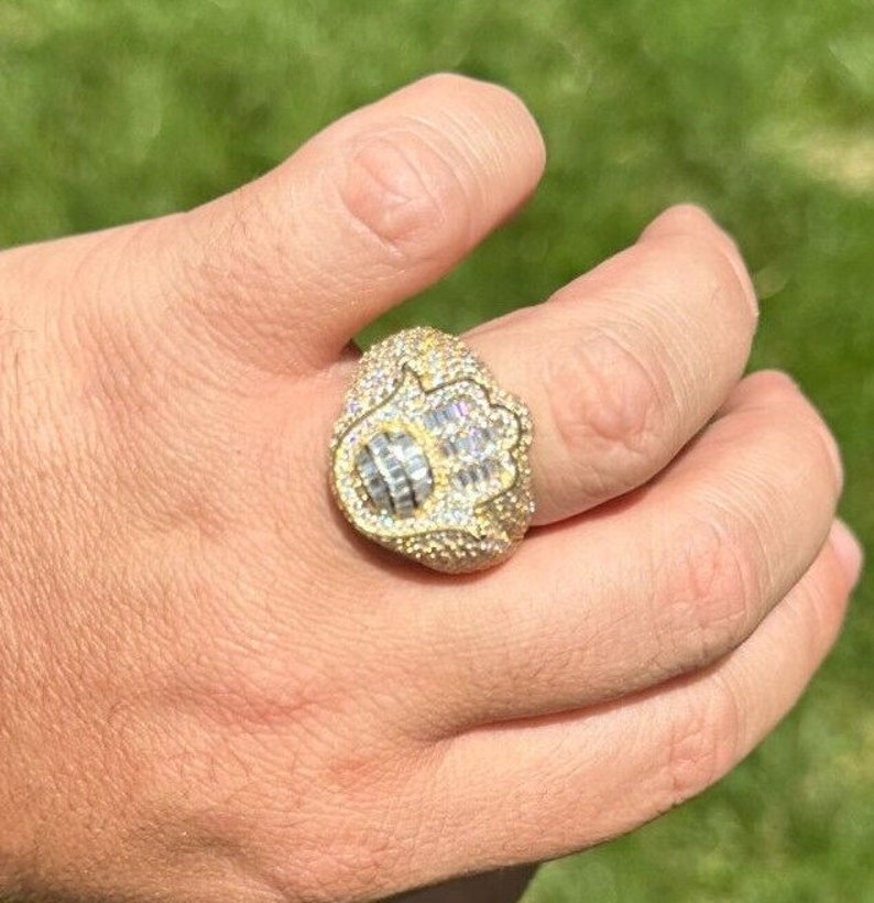 Puede incluir: Un anillo de oro con un dise&ntilde;o de mano de hamsa, incrustado con piedras de circonita c&uacute;bica transparentes.