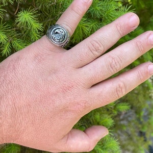 Puede incluir: Un anillo de plata con un dise&ntilde;o de &aacute;guila en la cara. El anillo se lleva en un dedo.