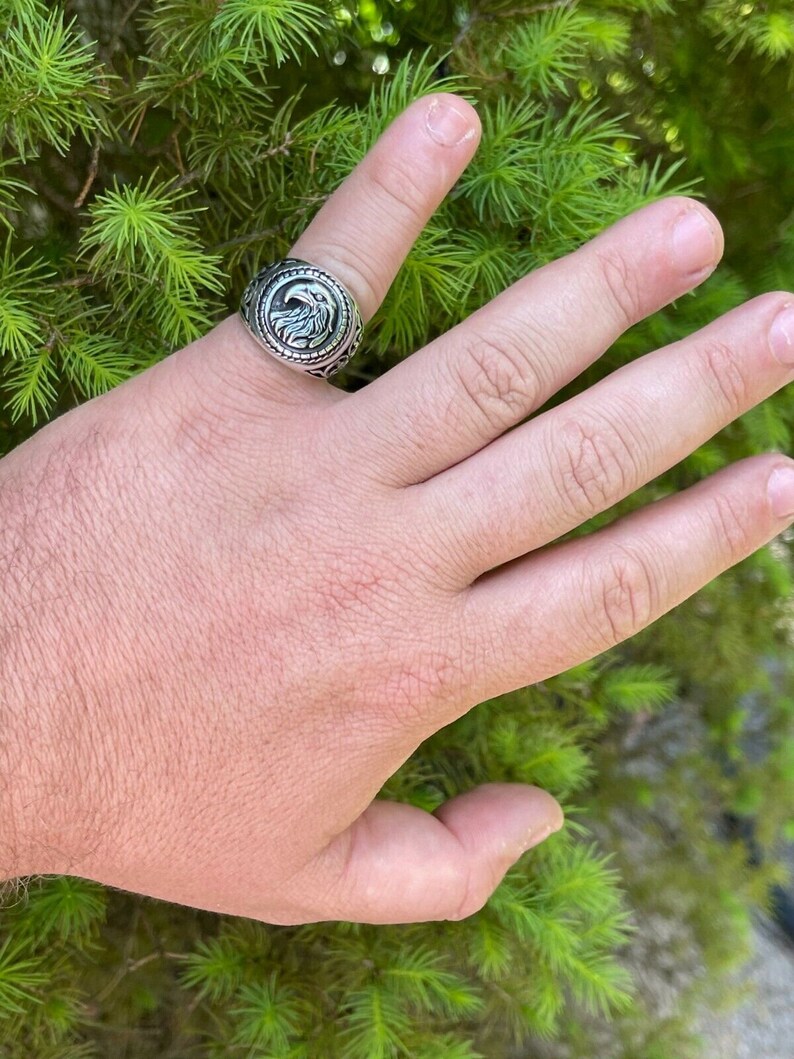 Puede incluir: Un anillo de plata con un dise&ntilde;o de &aacute;guila en la cara. El anillo se lleva en un dedo.