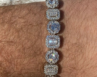 May include: A silver bracelet with a row of square-shaped links, each set with a large round clear stone surrounded by smaller clear stones.