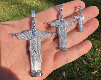 Puede incluir: Tres colgantes de plata con forma de la estatua del Cristo Redentor, cada uno de un tamaño diferente. Los colgantes están cubiertos de piedras transparentes brillantes.