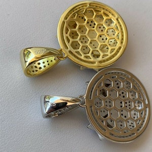 Puede incluir: Dos colgantes, uno dorado y otro plateado, con un dise&ntilde;o circular que presenta un patr&oacute;n de panal. Ambos colgantes tienen una anilla con la inscripci&oacute;n "925" en la parte posterior.