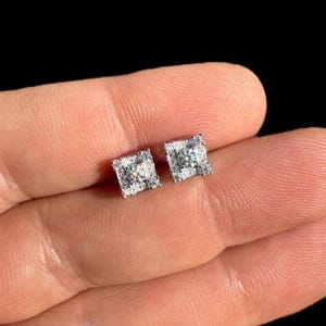 May include: A pair of silver square stud earrings with a clear cubic zirconia center stone and smaller stones surrounding the center stone.