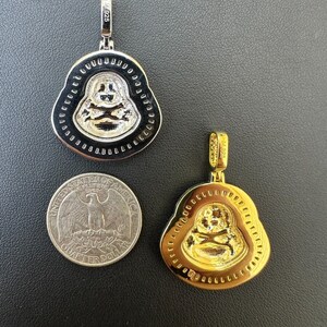 May include: Two Buddha pendant necklaces, one silver-toned and one gold-toned, with a quarter for size comparison. The pendants feature a smiling Buddha design with a skull and crossbones. The silver pendant is marked "M925".