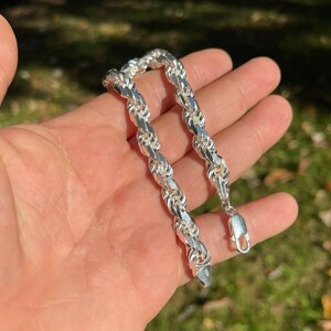 Puede incluir: Un brazalete de cadena de cuerda de plata con cierre de langosta. El brazalete est&aacute; hecho de una cadena gruesa y trenzada.