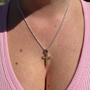 May include: A silver rope chain necklace with a small cross pendant. The cross is set with yellow cubic zirconia stones.