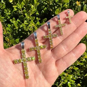 May include: Five silver cross pendants with yellow cubic zirconia stones. The crosses are of different sizes and are arranged in a row on a hand.