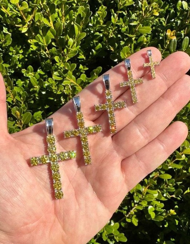 May include: Five silver cross pendants with yellow cubic zirconia stones. The crosses are of different sizes and are arranged in a row on a hand.