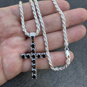 May include: A silver rope chain necklace with a black diamond cross pendant.