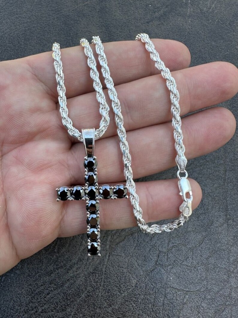 May include: A silver rope chain necklace with a black diamond cross pendant.