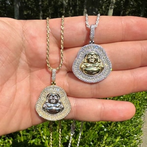 May include: Two Buddha pendant necklaces. One has a gold chain and pendant with a silver Buddha and a halo of clear stones. The other has a silver chain and pendant with a gold Buddha and a halo of clear stones.