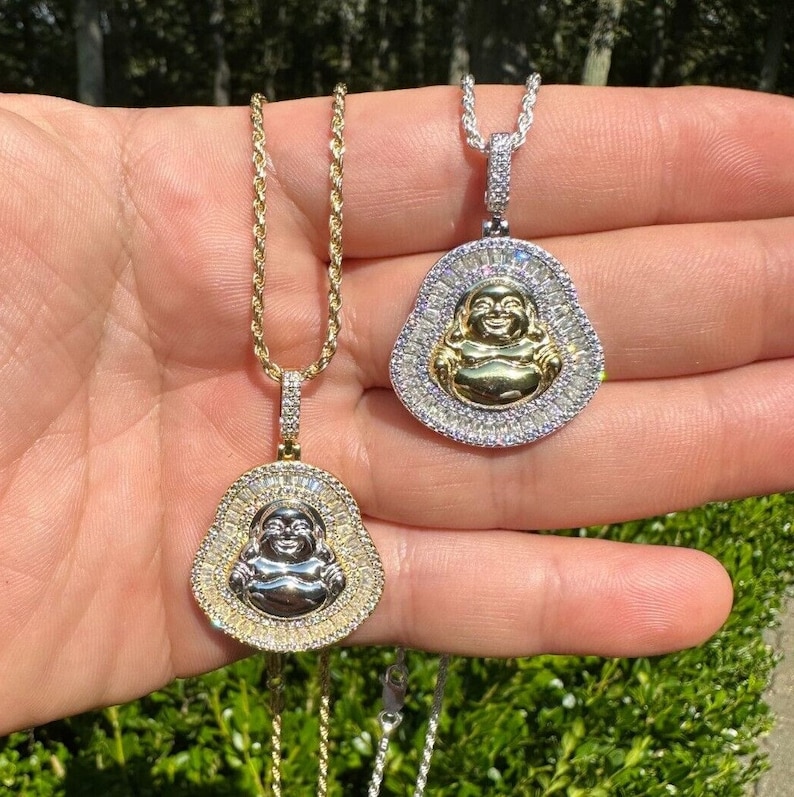 May include: Two Buddha pendant necklaces. One has a gold chain and pendant with a silver Buddha and a halo of clear stones. The other has a silver chain and pendant with a gold Buddha and a halo of clear stones.