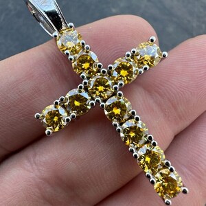 May include: A silver cross pendant with a yellow cubic zirconia stone encrusted design.