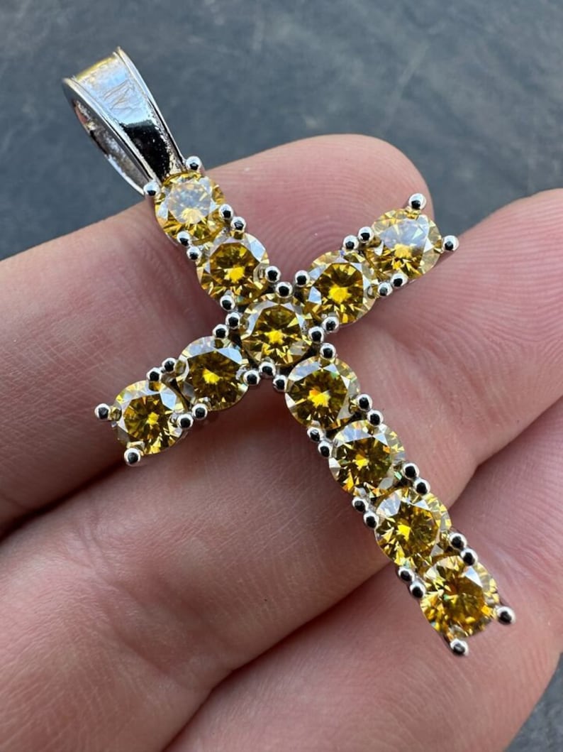 May include: A silver cross pendant with a yellow cubic zirconia stone encrusted design.