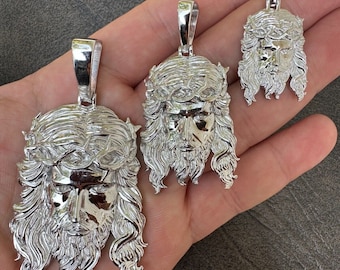 May include: Three silver pendants featuring a detailed depiction of Jesus' face with a crown of thorns. The pendants are of varying sizes and are displayed on a hand.