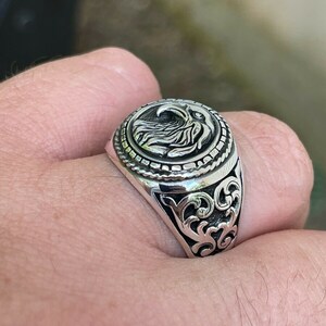 Puede incluir: Un anillo de plata con un dise&ntilde;o de &aacute;guila en la parte superior. El anillo tiene un dise&ntilde;o detallado y adornado en la banda.