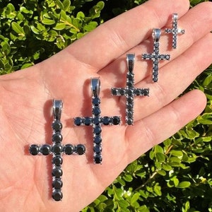 May include: Five silver cross pendants with black cubic zirconia stones. The crosses are of different sizes and are arranged in a row on a hand.