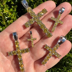 May include: Four silver cross pendants with yellow cubic zirconia stones. The crosses are of different sizes.