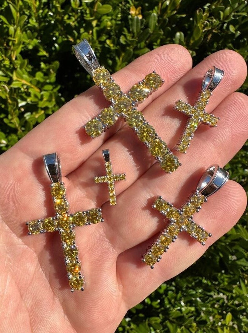 May include: Four silver cross pendants with yellow cubic zirconia stones. The crosses are of different sizes.
