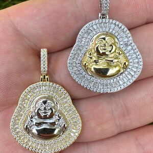 May include: Two gold and silver Buddha pendant necklaces. Each pendant features a smiling Buddha figure surrounded by a halo of baguette-cut stones. The pendants are suspended from diamond-studded bails.
