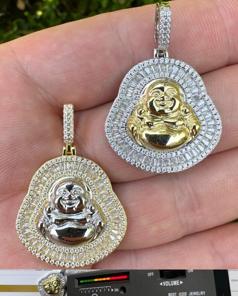 May include: Two gold and silver Buddha pendant necklaces. Each pendant features a smiling Buddha figure surrounded by a halo of baguette-cut stones. The pendants are suspended from diamond-studded bails.