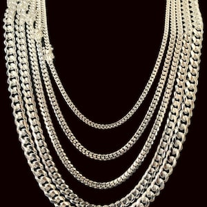 May include: Five silver Cuban link chains of varying widths, layered on a black background.