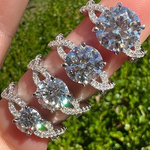 May include: Four silver engagement rings with large, clear, round diamonds set in a twisted band design. The rings are arranged in size order, with the largest ring at the top and the smallest ring at the bottom.