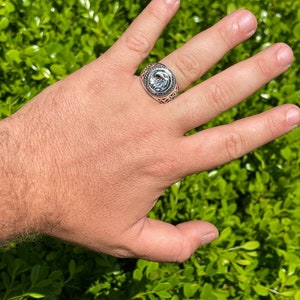 Puede incluir: Un anillo de plata con un dise&ntilde;o intrincado que presenta una cabeza de &aacute;guila estilizada. El anillo se lleva en un dedo.
