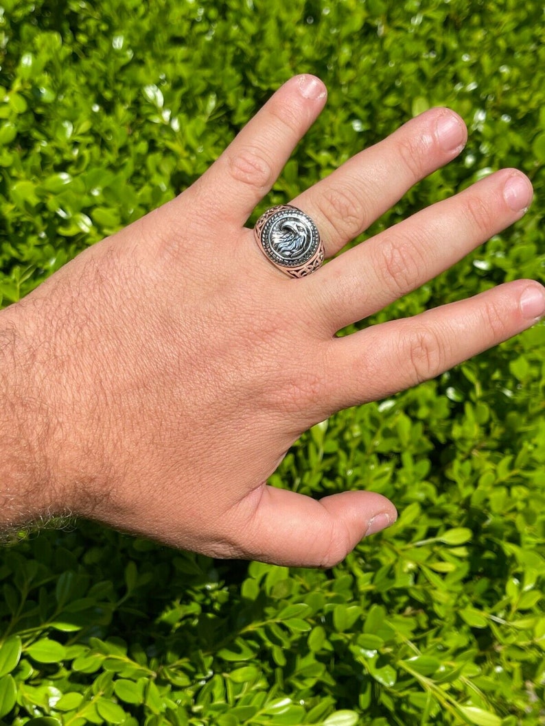 Puede incluir: Un anillo de plata con un dise&ntilde;o intrincado que presenta una cabeza de &aacute;guila estilizada. El anillo se lleva en un dedo.