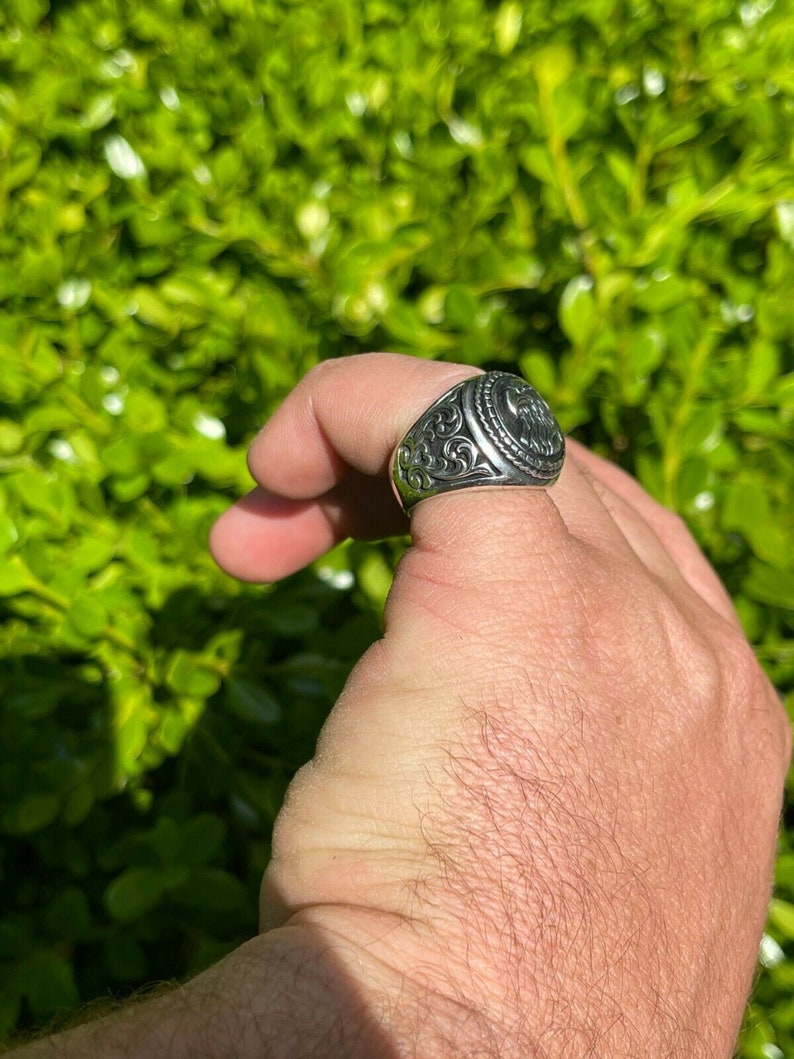 Puede incluir: Un anillo de plata con un dise&ntilde;o adornado y una pieza central circular elevada. El anillo est&aacute; en un dedo.